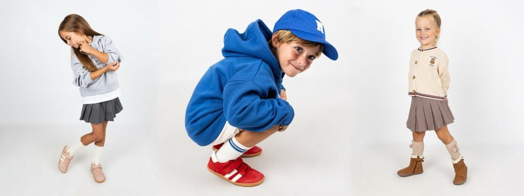 Tres niños posando con diferentes estilos de calzado barefoot: zapatillas deportivas flexibles rojas y rosas, y botas minimalistas marrones con puntera ancha.